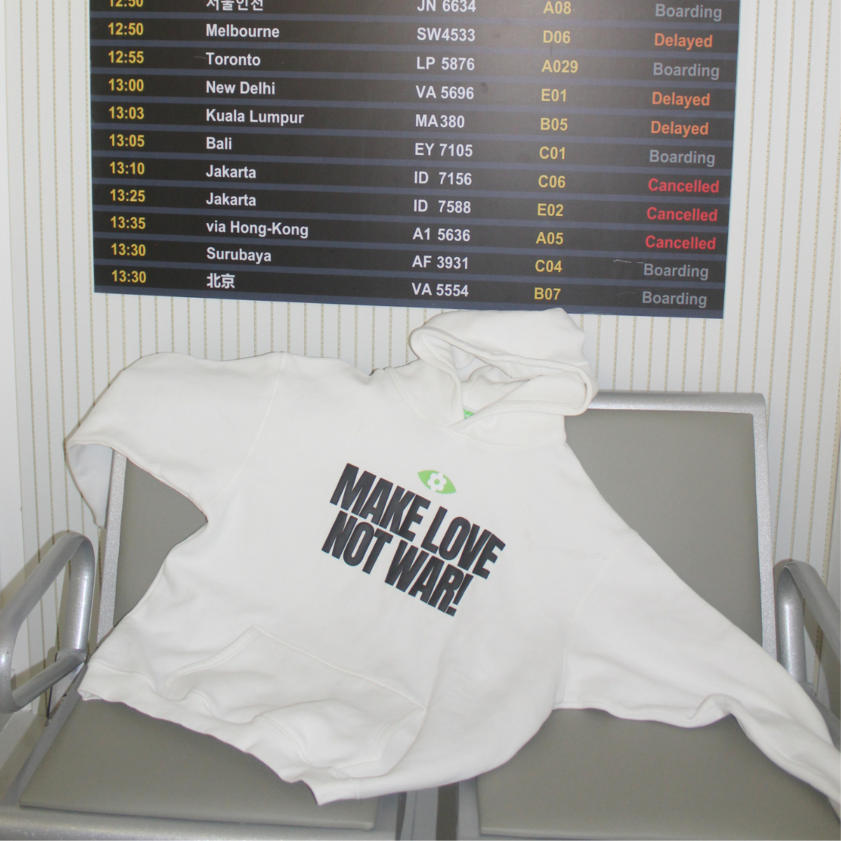 Herblunt White hoodie with 'Make Love Not War' text draped over a chair in front of an airport departure board.